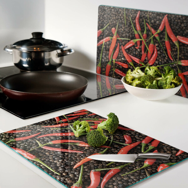 Tagliere in vetro con decorazione di peperoncini su sfondo effetto pepe nero